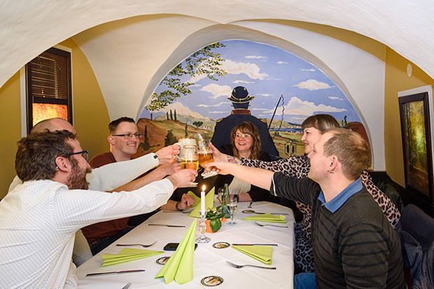 Prost! Auf einen gemütlichen Abend in der Alten Post. Freunde stoßen mit einem Glas Bier in einer Nische des Gasthauses an